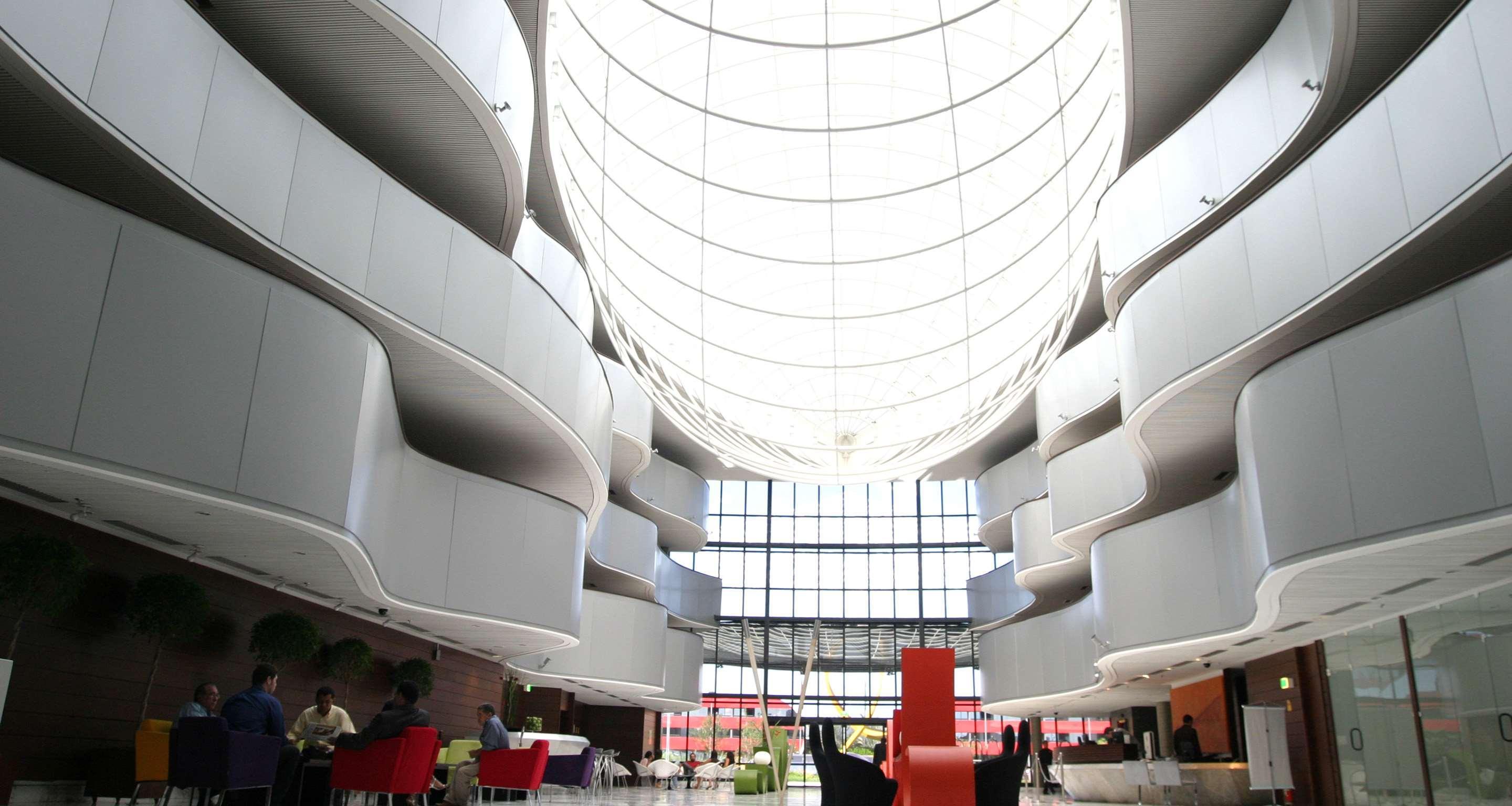 Royal Tulip Brasilia Alvorada Hotell Exteriör bild The photo depicts a modern interior space characterized by sleek, curvilinear architecture. The ceiling features a large, dome-like skylight that allows natural light to flood the area. The walls display a minimalist design with smooth, white surface